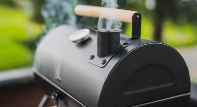 A meat smoker with the lid closed and smoke coming from the chimney