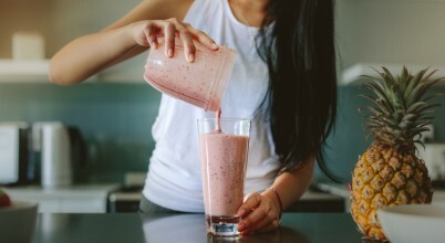 A woman pours a homemade fruit smoothie into a glass