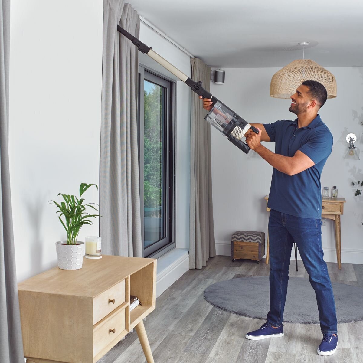 A man vacuums curtains with a Shark brand vacuum cleaner.