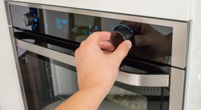 A hand turning a control dial to change the settings on a modern built-in wall oven