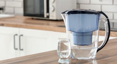 A water filter jug with a glass of water on a kitchen benchtop