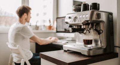 A domestic coffee machine in a home environment with a man working at a desk on a computer