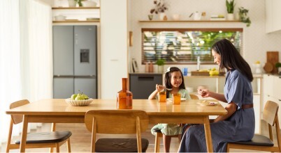A smiling woman and child eating at a kitchen dining table with Haier appliances in the background