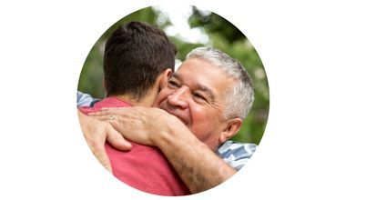 A smiling older man hugs his adult son